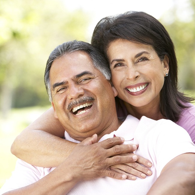 Pareja sonriendo abrazándose mientras está afuera